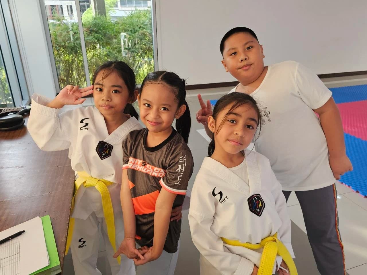 Four young students in white dobok, two flashing peace signs at the camera before class