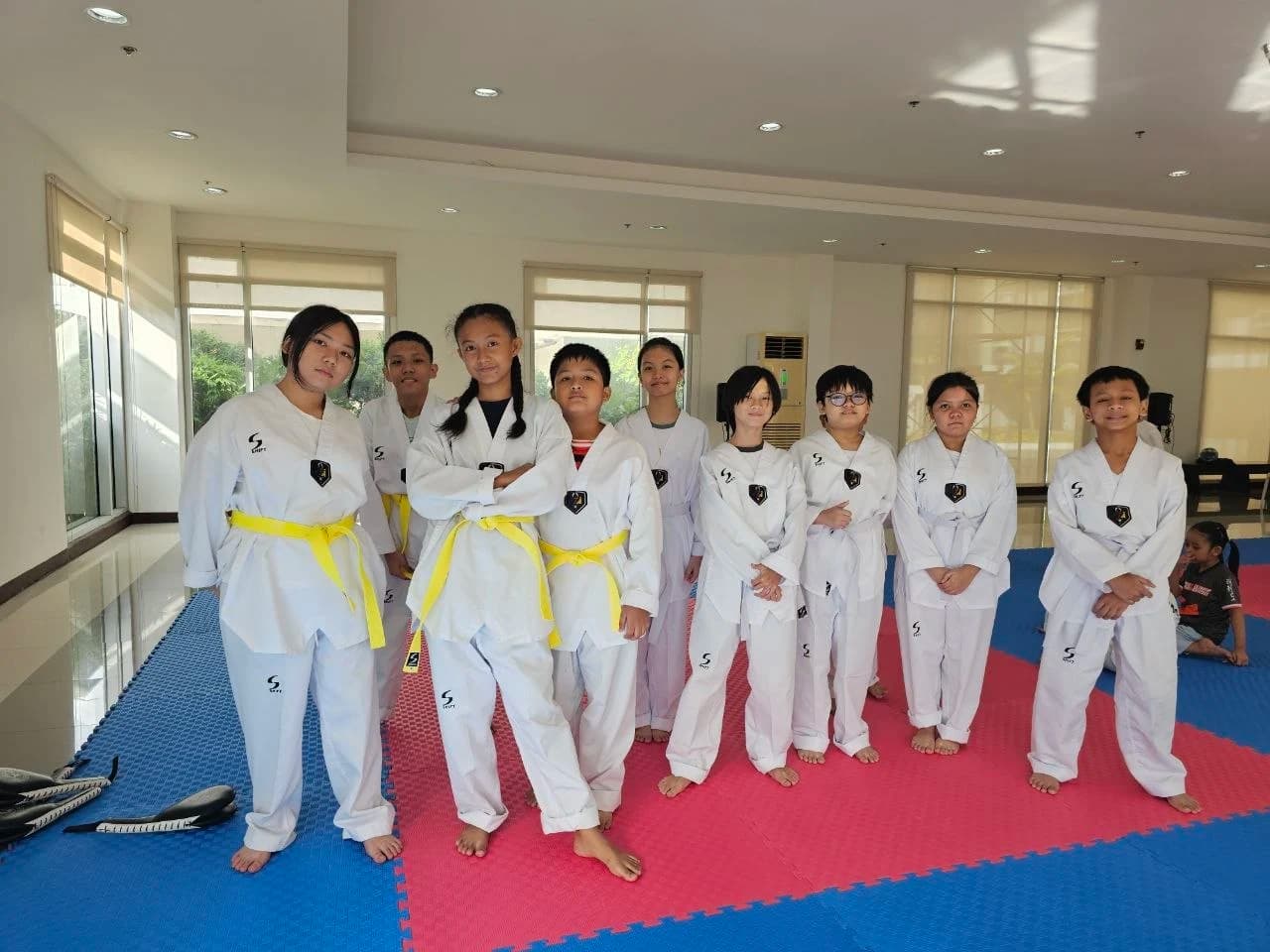 Ten students in dobok and yellow belts standing together on the blue and red mat