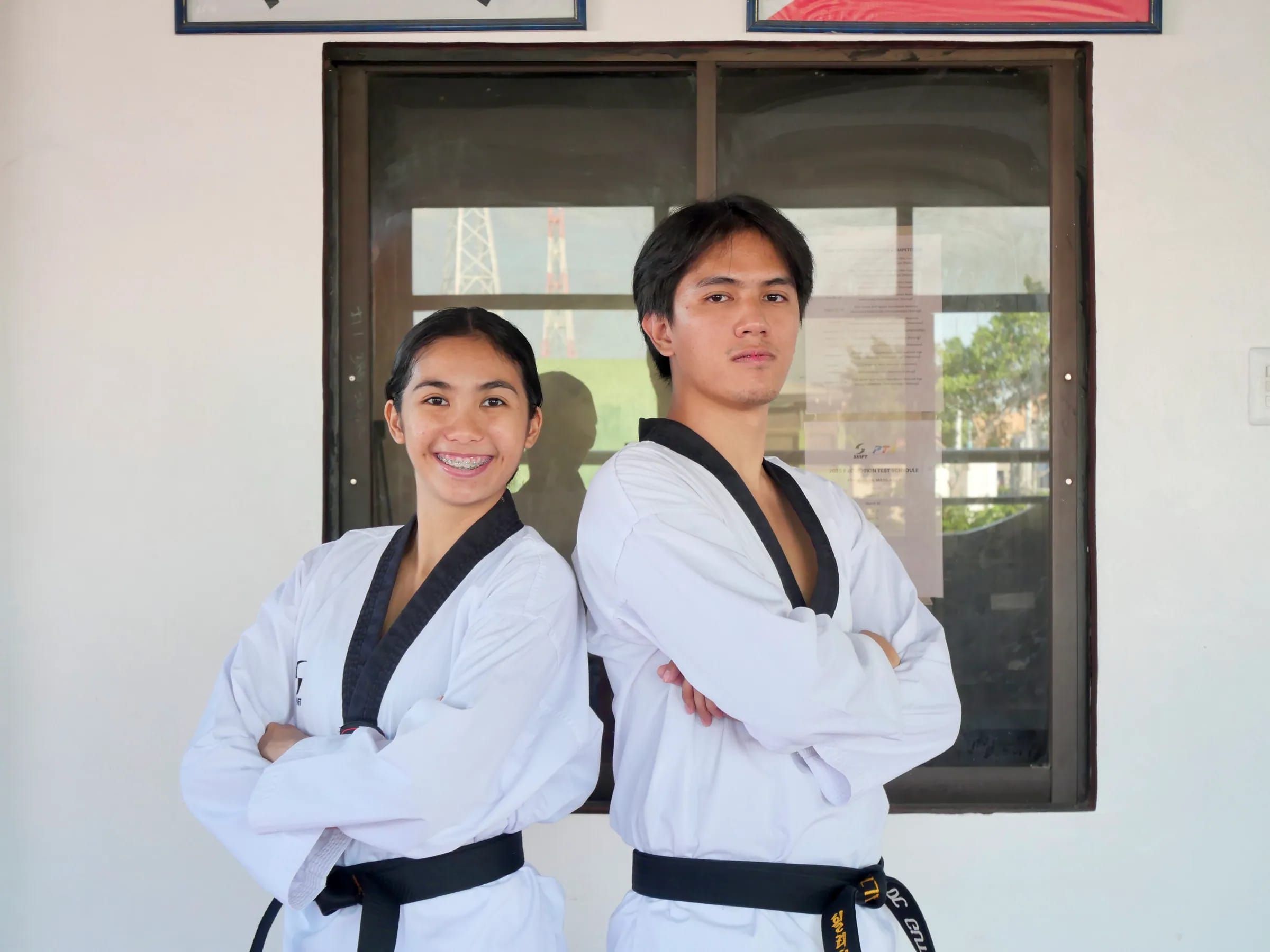 Coach Nica and Coach Gian standing back to back with arms crossed, in black-belt doboks