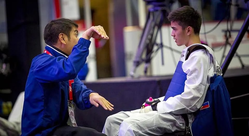 Coach Gian in sparring gear, receiving instructions from a coach at a competition