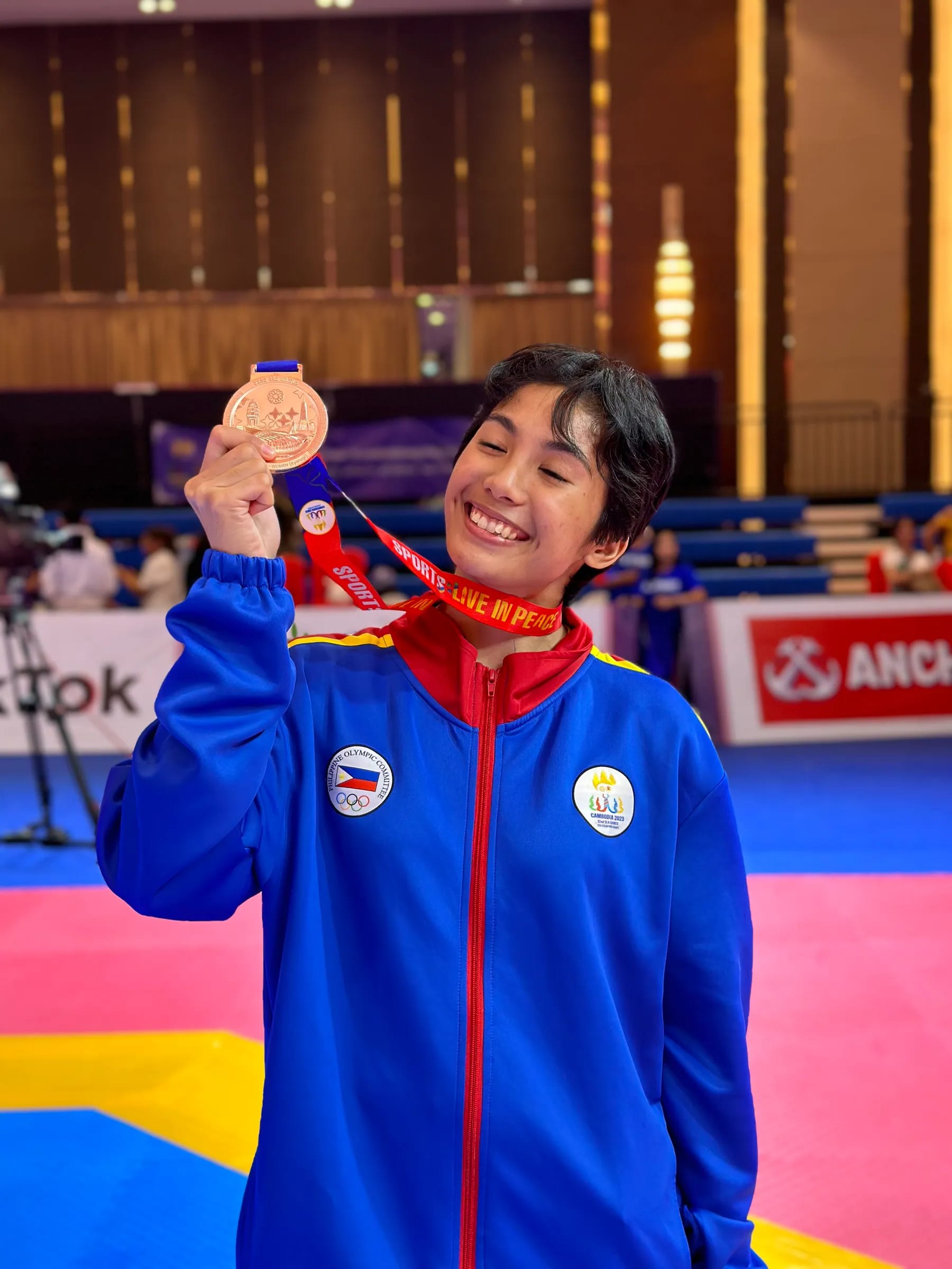 Coach Nica in a Philippine national team jacket, holding up a medal