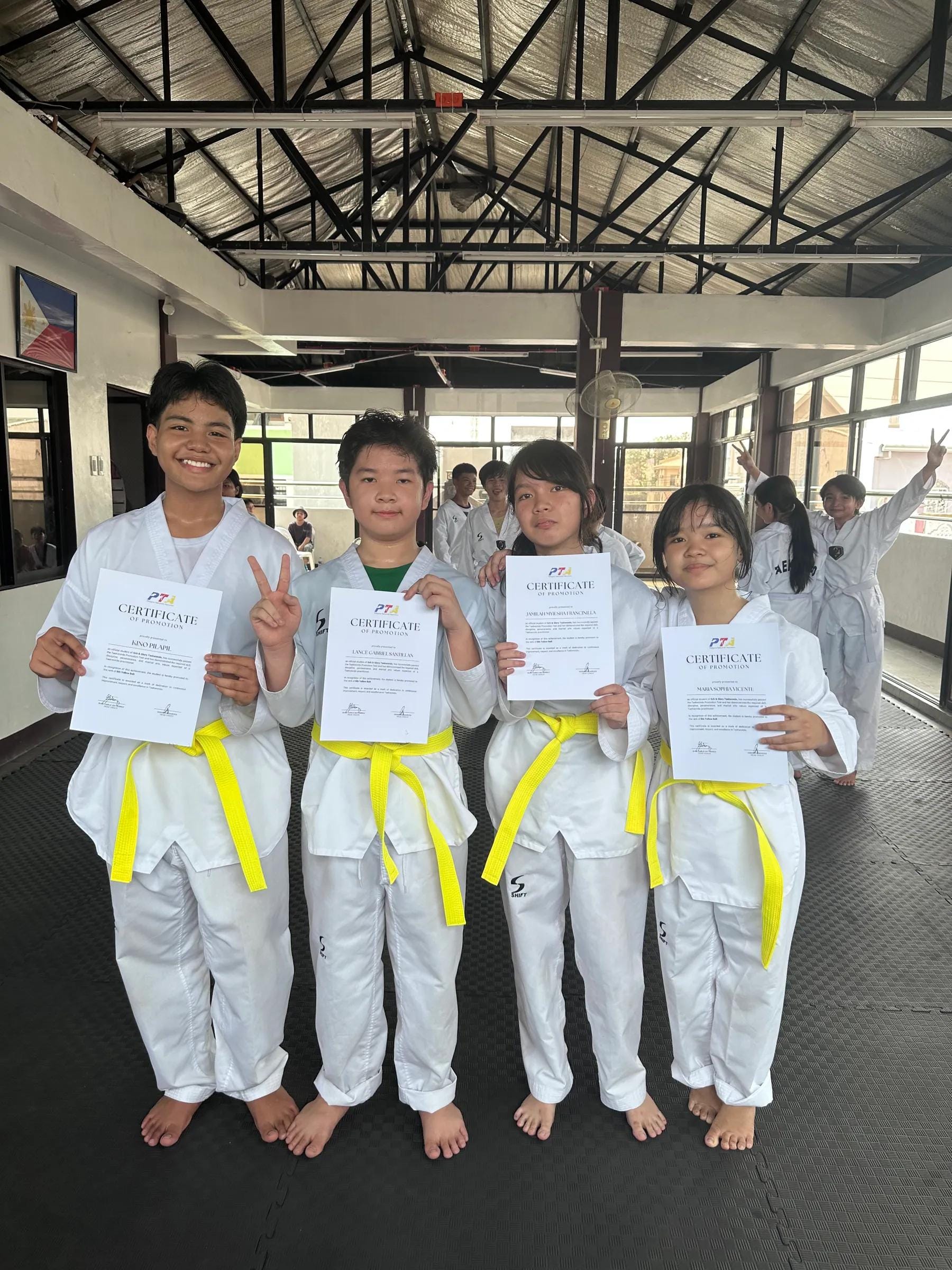Four students holding their grading certificates, wearing new yellow belts