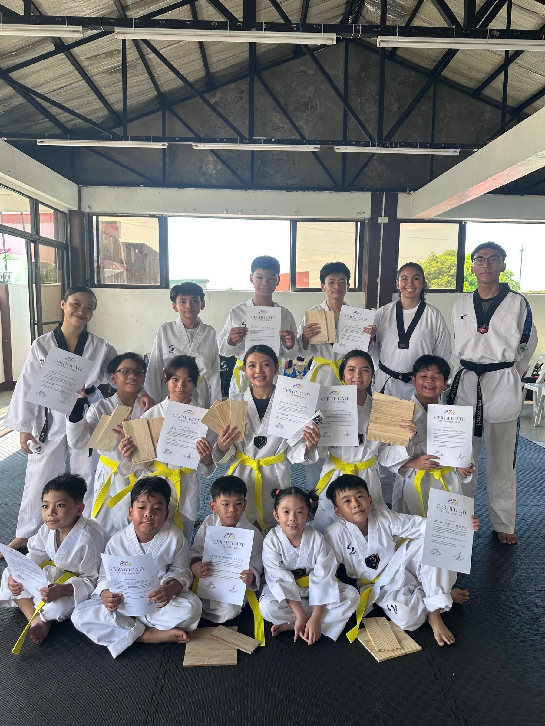 Students holding grading certificates in a group photo at the open-air training hall