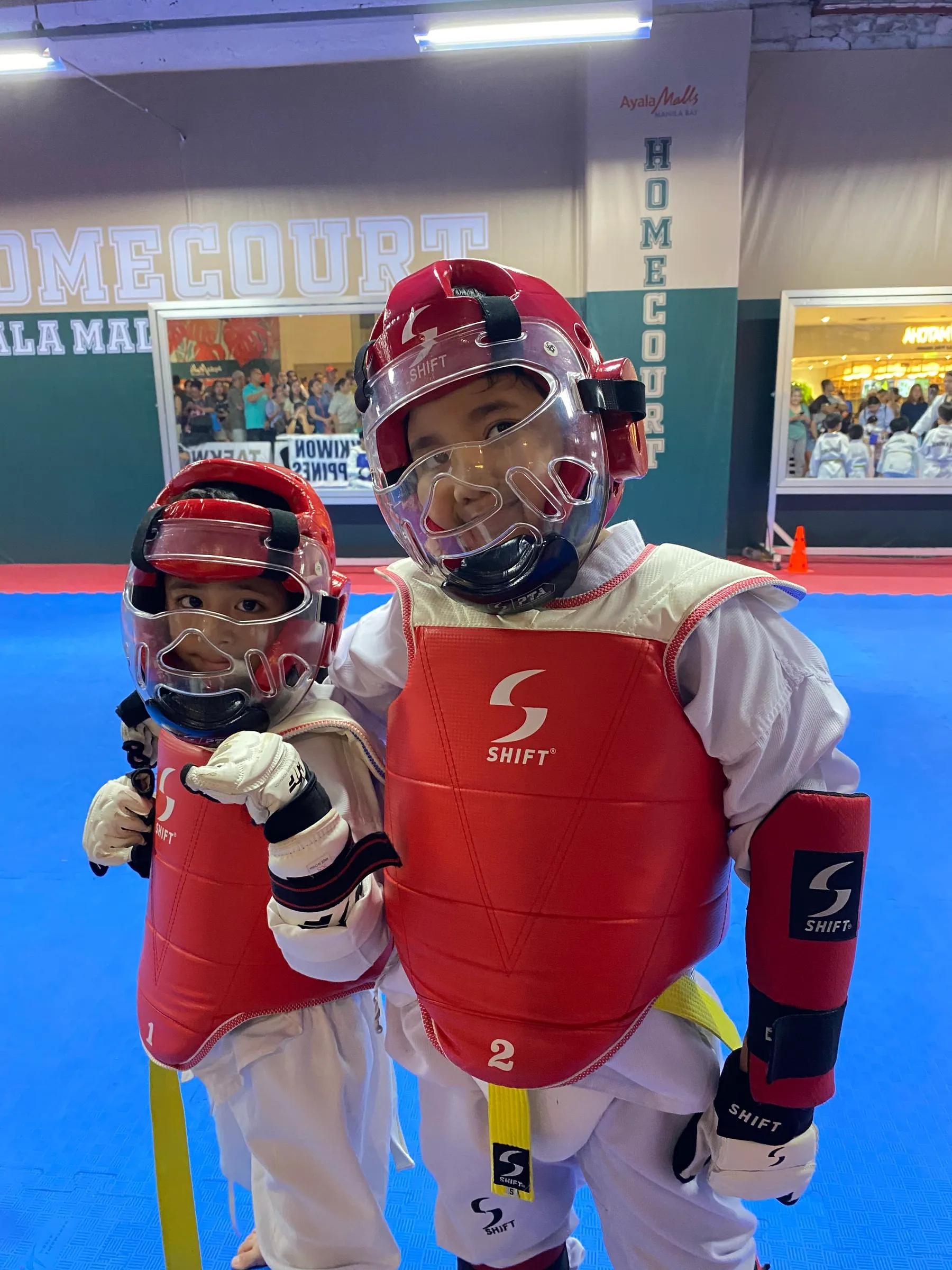 Two young students in full sparring gear — head guards, chest protectors and gloves
