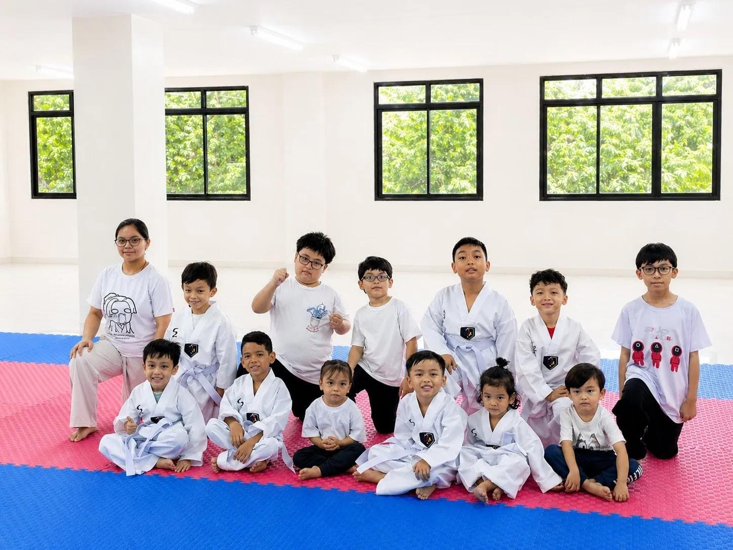 Students in white t-shirts and doboks seated together on the mat