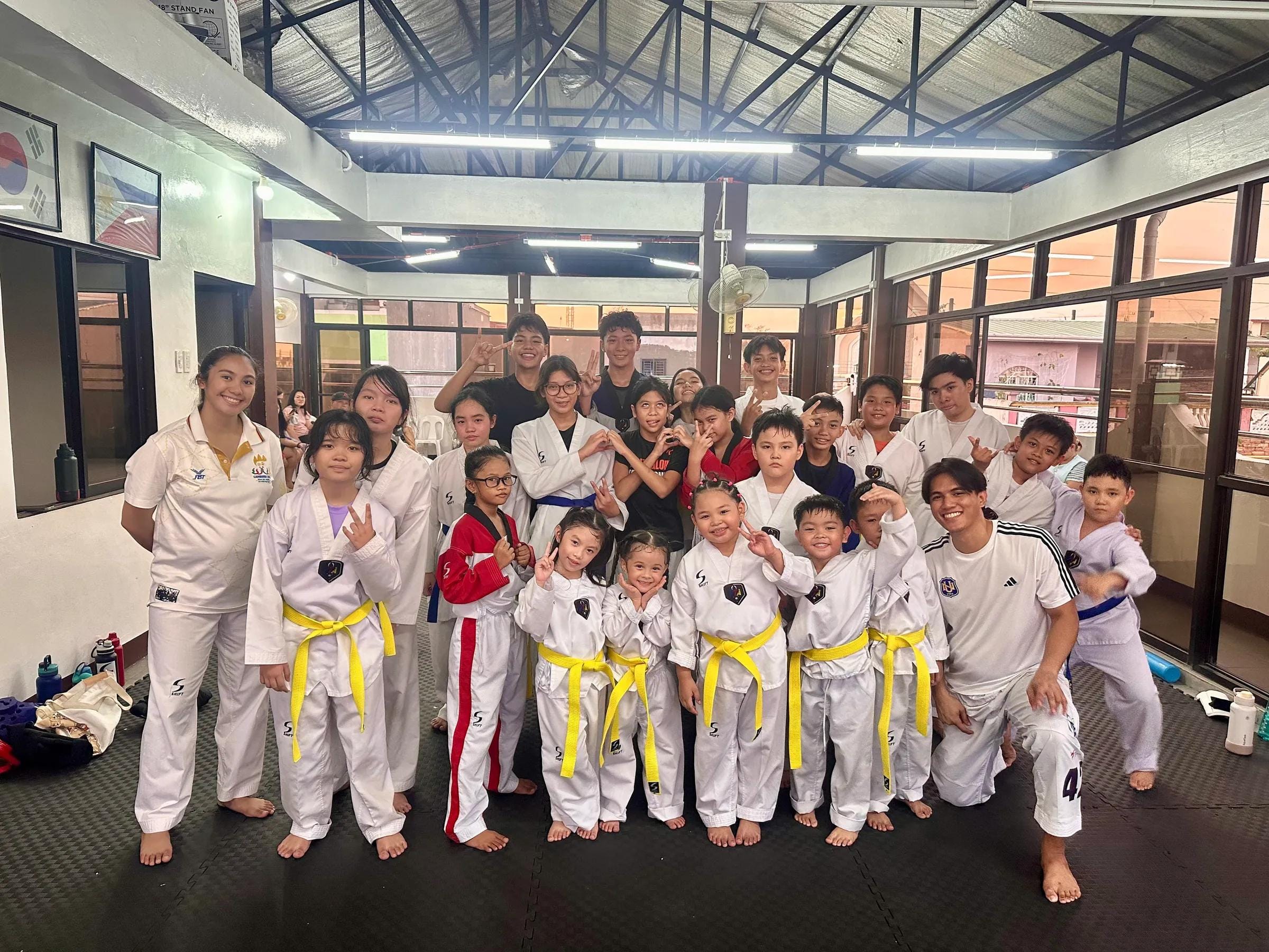 A large group of yellow-belt students and coaches in the open-air training hall