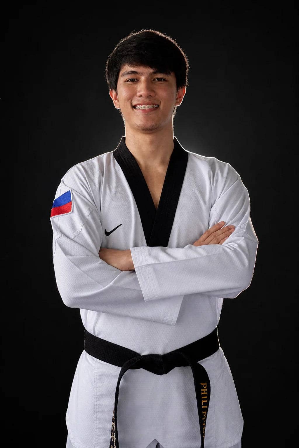 Coach Gian in a black-belt dobok with a Philippine flag patch, arms crossed