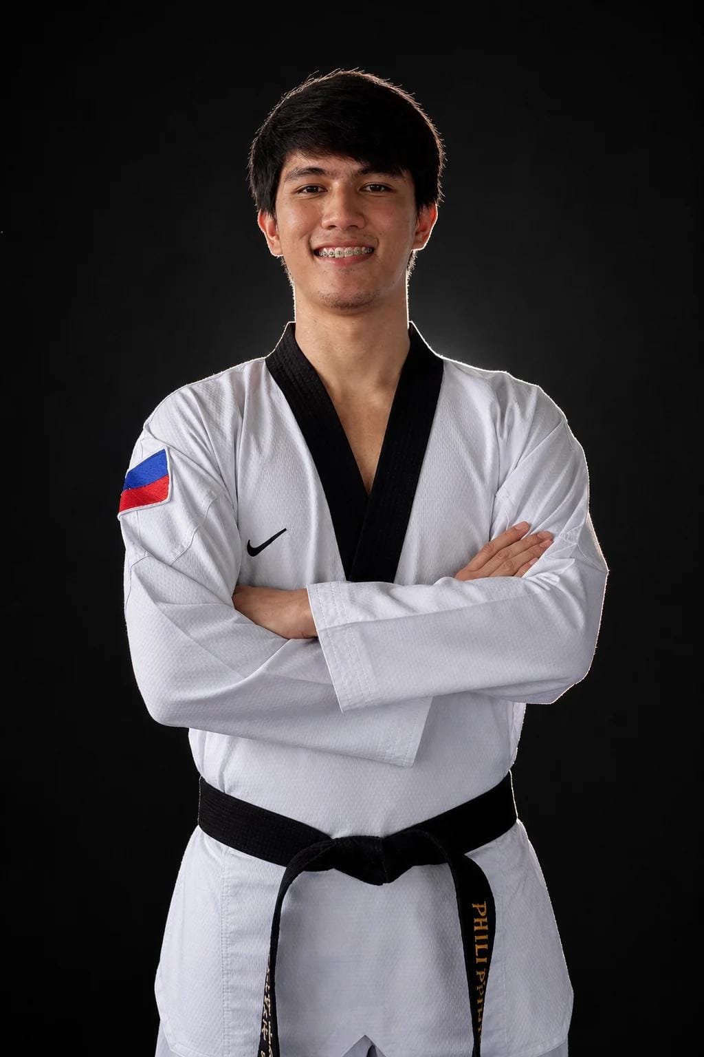 Coach Gian in a black-belt dobok with a Philippine flag patch, arms crossed