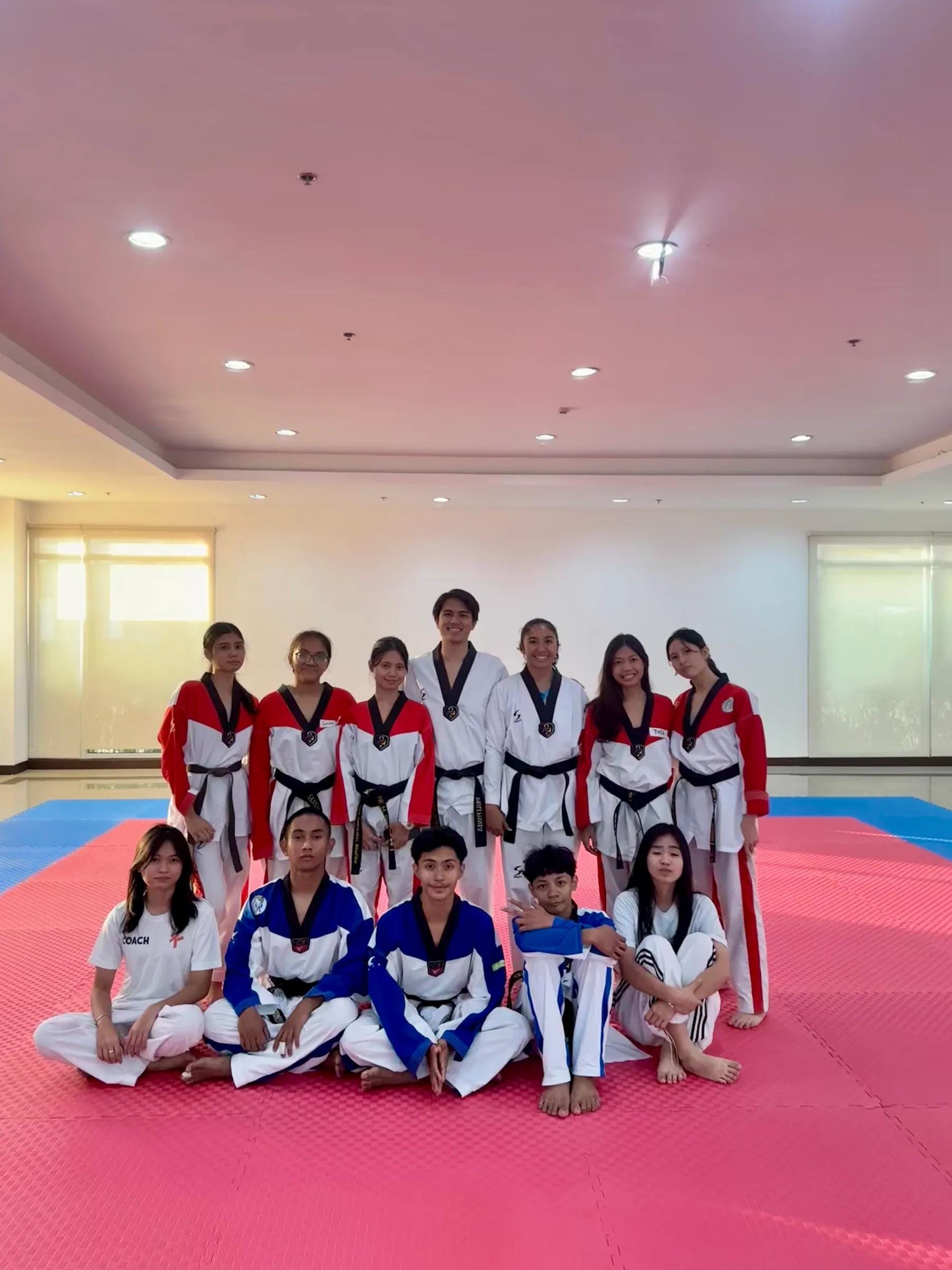 Teen and adult students seated and standing together on the mat