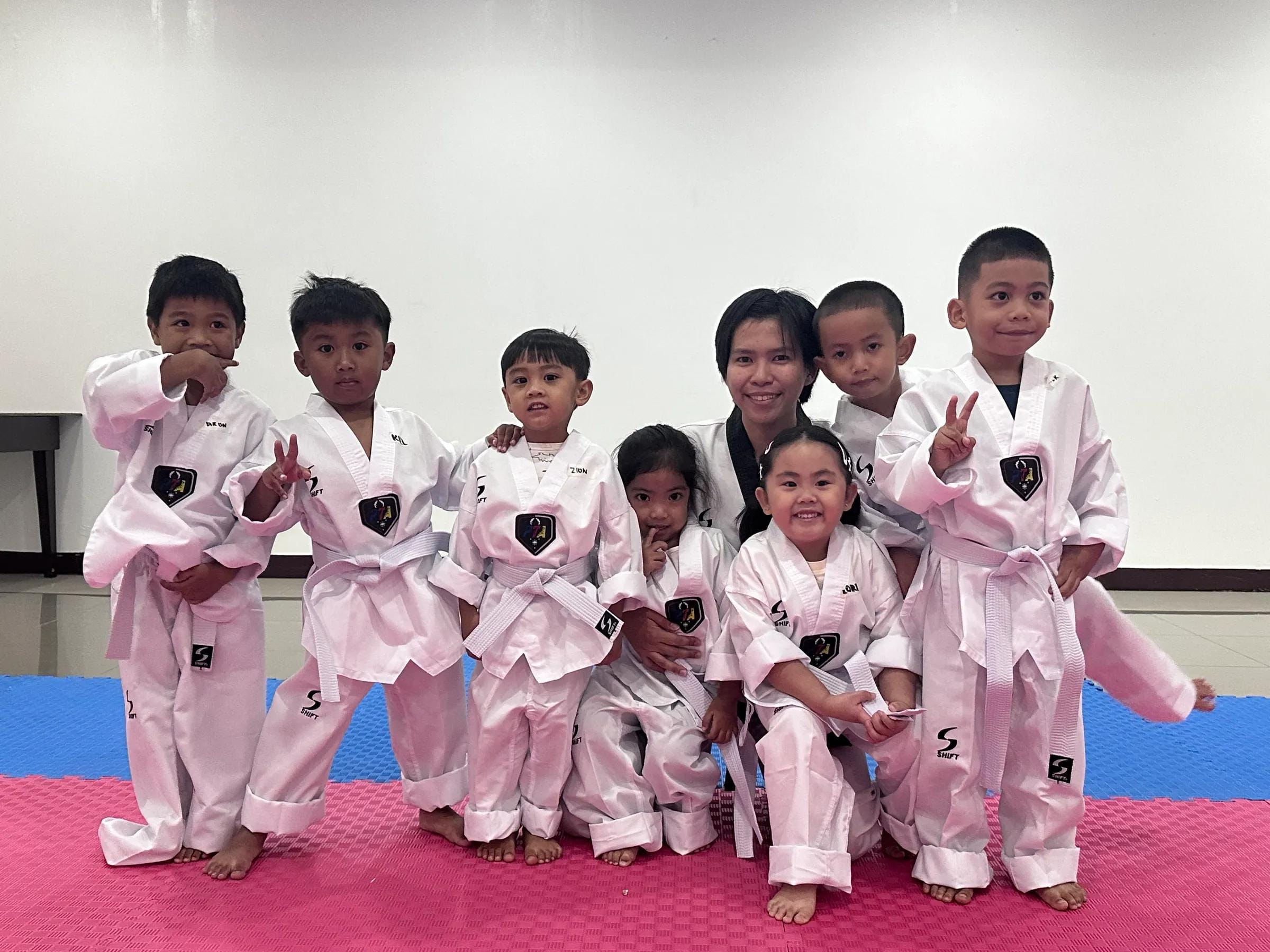 Little Tigers in white doboks posing together, several flashing peace signs